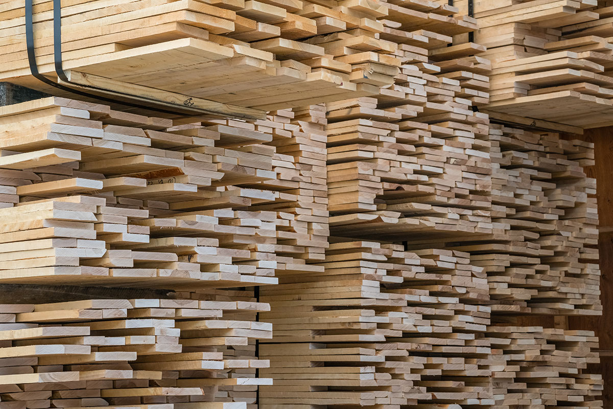Stacks of planed lumber boards piled high on racks in a timber warehouse, some bundles held with black strapping