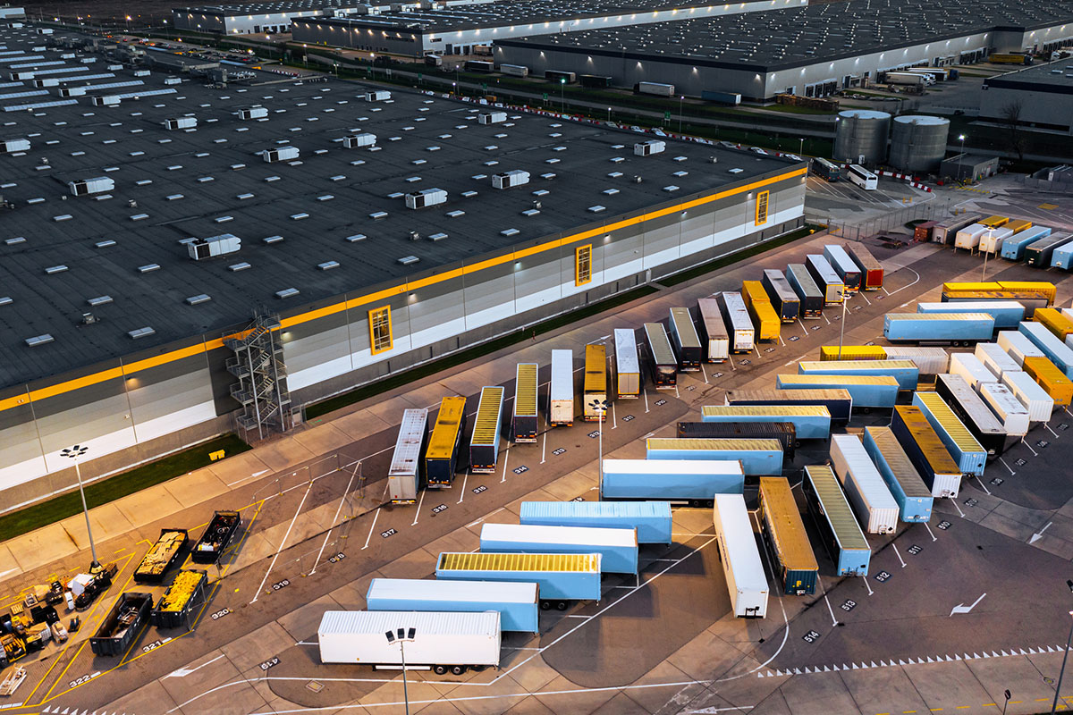 Aerial view of rows of parked semi trailers beside a large distribution center at dusk