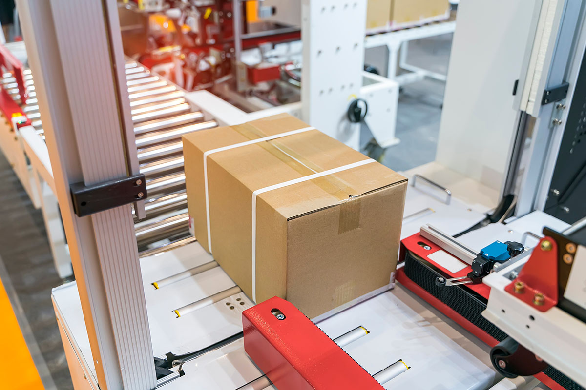 Sealed cardboard carton with white strapping moving through an automated packing line in a manufacturing plant