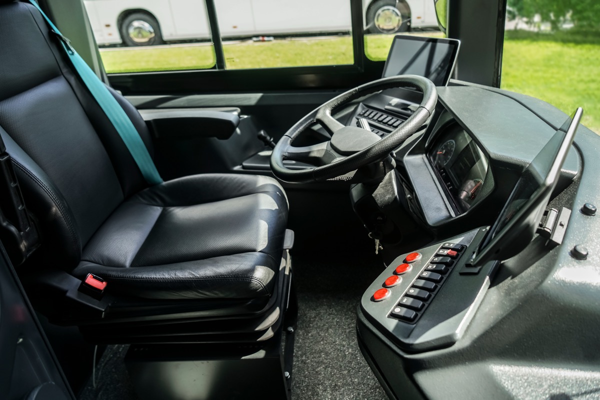 Empty driver's seat and steering wheel inside a commercial vehicle cab with a monitor mounted beside the dashboard