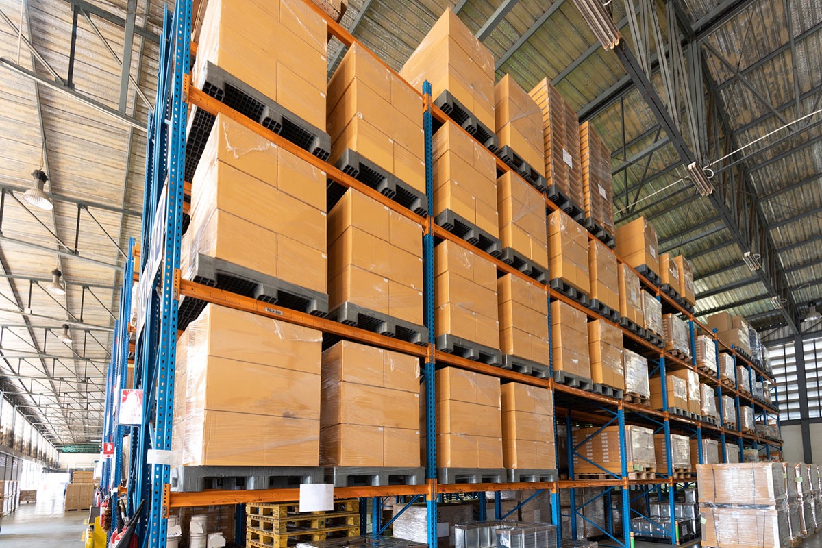 Tall blue and orange pallet racking loaded with shrink-wrapped cartons inside a large warehouse