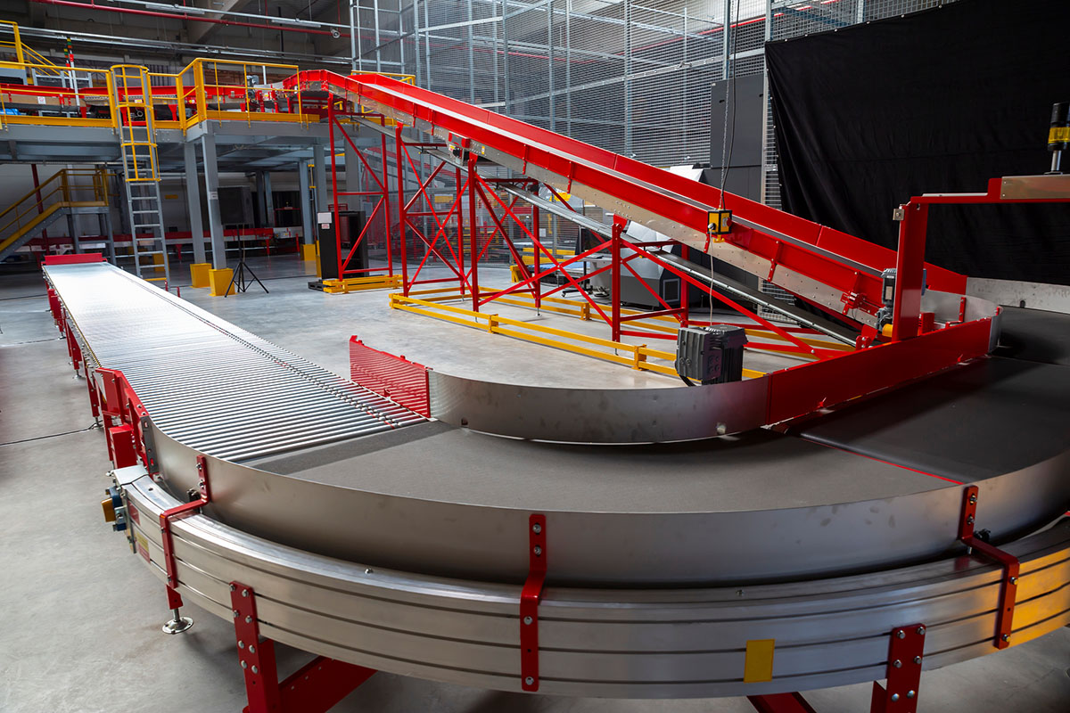 Empty curved parcel sortation conveyor with a red inclined belt inside a modern distribution center