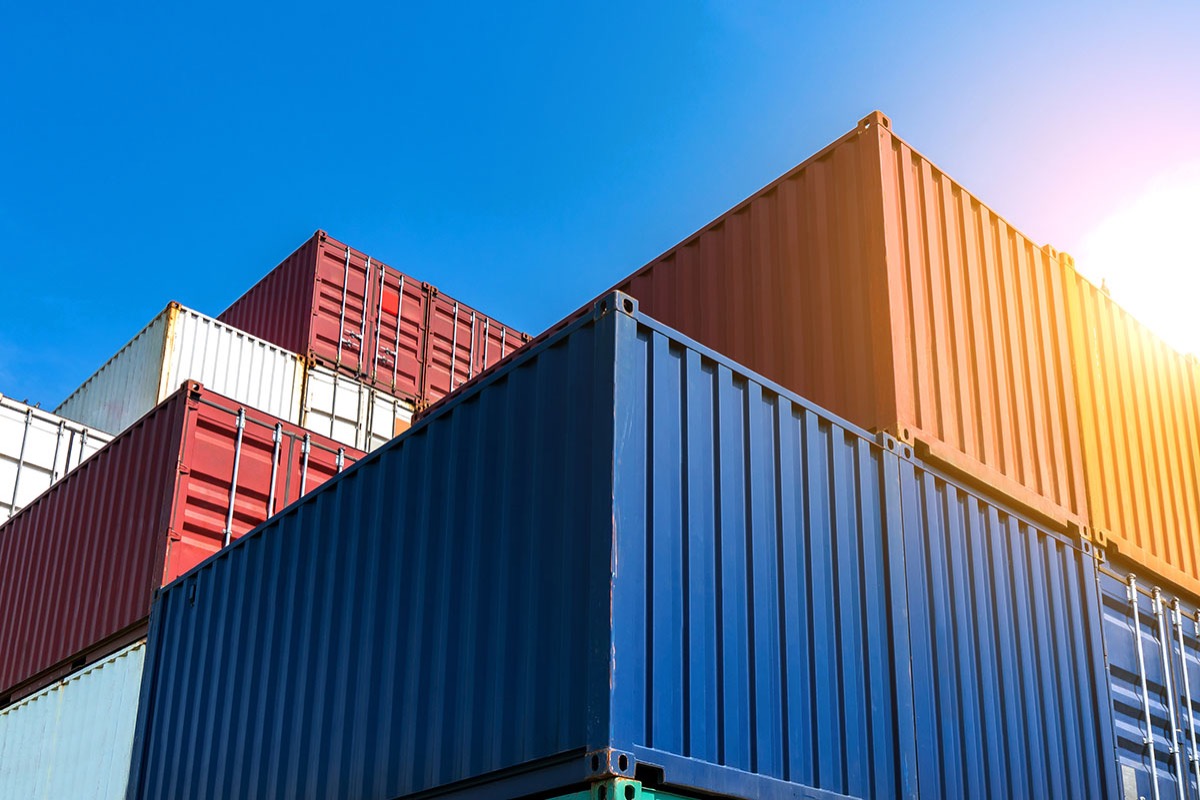 Stacked blue, red and orange shipping containers rising against a clear blue sky in a container yard